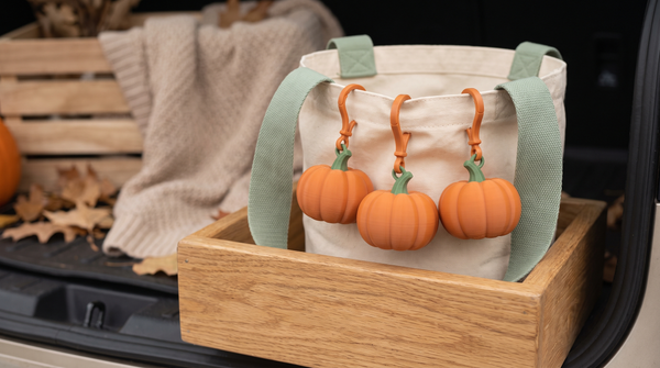 Small 3D printed pumpkin bag charms clipped to a trick-or-treat bucket on a car tailgate