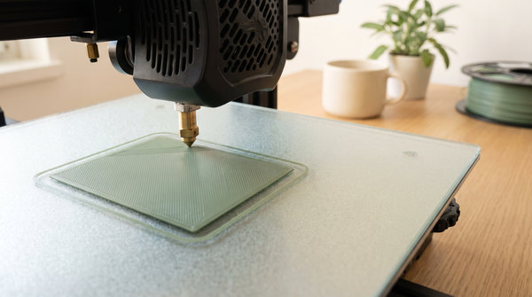 Macro of a 3D printer first layer being laid down on a textured build plate, nozzle in motion