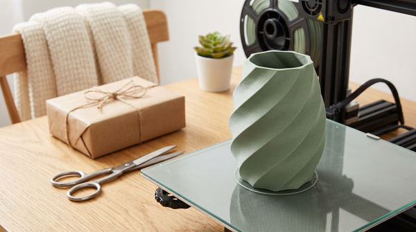 A fast simple 3D printed gift item fresh off the bed beside a wrapped box and scissors