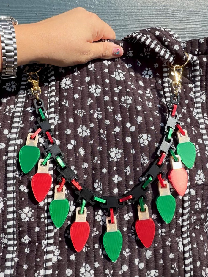 3D printed Christmas lights purse charm chain with red and green bulbs clipped to a floral tote bag